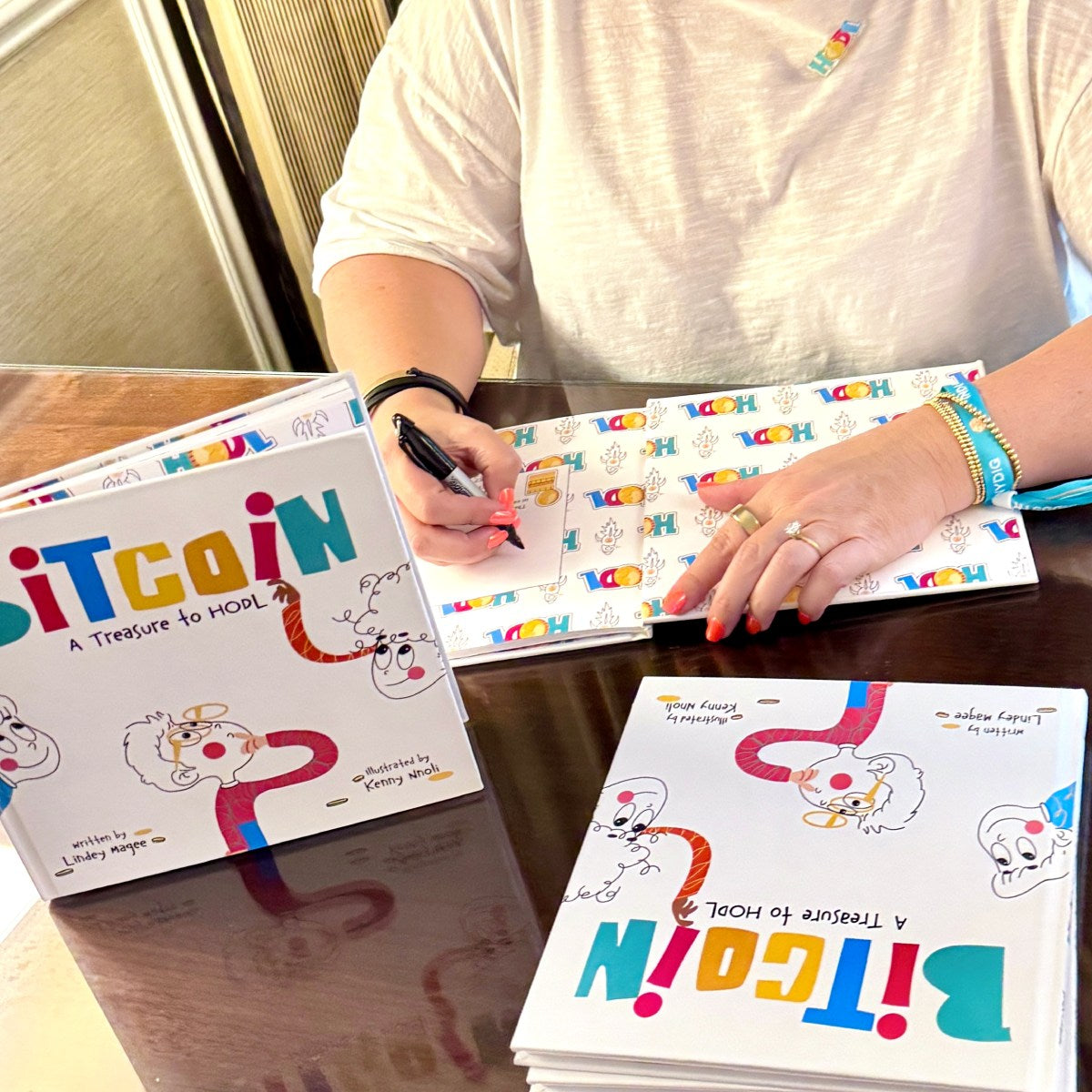 Lindey Magee (Author) signing the book titled 'Bitcoin: A Treasure to Hold' with colorful pages.
